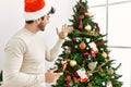 Young hispanic man smiling happy decorating christmas tree at home