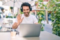 Young hispanic man smiling happy doing video call using laptop and headphones at coffee shop terrace Royalty Free Stock Photo