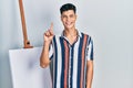 Young hispanic man standing close to empty canvas showing and pointing up with finger number one while smiling confident and happy Royalty Free Stock Photo