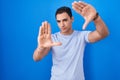 Young hispanic man standing over blue background doing frame using hands palms and fingers, camera perspective Royalty Free Stock Photo