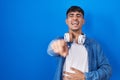 Young hispanic man standing over blue background laughing at you, pointing finger to the camera with hand over body, shame Royalty Free Stock Photo