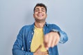 Young hispanic man standing over blue background laughing at you, pointing finger to the camera with hand over body, shame Royalty Free Stock Photo