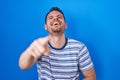 Young hispanic man standing over blue background laughing at you, pointing finger to the camera with hand over body, shame Royalty Free Stock Photo