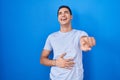 Young hispanic man standing over blue background laughing at you, pointing finger to the camera with hand over body, shame Royalty Free Stock Photo