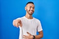 Young hispanic man standing over blue background laughing at you, pointing finger to the camera with hand over body, shame Royalty Free Stock Photo