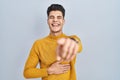 Young hispanic man standing over blue background laughing at you, pointing finger to the camera with hand over body, shame Royalty Free Stock Photo