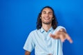 Young hispanic man standing over blue background laughing at you, pointing finger to the camera with hand over body, shame Royalty Free Stock Photo