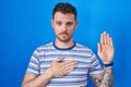 Young hispanic man standing over blue background swearing with hand on chest and open palm, making a loyalty promise oath Royalty Free Stock Photo