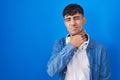 Young hispanic man standing over blue background touching painful neck, sore throat for flu, clod and infection