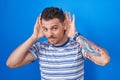 Young hispanic man standing over blue background trying to hear both hands on ear gesture, curious for gossip Royalty Free Stock Photo