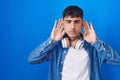 Young hispanic man standing over blue background trying to hear both hands on ear gesture, curious for gossip Royalty Free Stock Photo