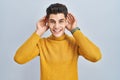 Young hispanic man standing over blue background trying to hear both hands on ear gesture, curious for gossip