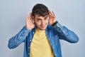 Young hispanic man standing over blue background trying to hear both hands on ear gesture, curious for gossip Royalty Free Stock Photo