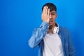 Young hispanic man standing over blue background yawning tired covering half face, eye and mouth with hand Royalty Free Stock Photo