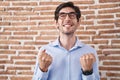 Young hispanic man standing over brick wall background excited for success with arms raised and eyes closed celebrating victory Royalty Free Stock Photo