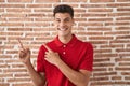 Young hispanic man standing over bricks wall smiling and looking at the camera pointing with two hands and fingers to the side Royalty Free Stock Photo