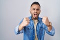 Young hispanic man standing over isolated background angry and mad raising fists frustrated and furious while shouting with anger