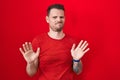 Young hispanic man standing over red background moving away hands palms showing refusal and denial with afraid and disgusting Royalty Free Stock Photo