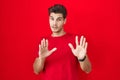 Young hispanic man standing over red background moving away hands palms showing refusal and denial with afraid and disgusting Royalty Free Stock Photo