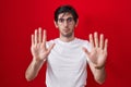 Young hispanic man standing over red background moving away hands palms showing refusal and denial with afraid and disgusting Royalty Free Stock Photo