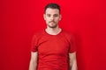 Young hispanic man standing over red background relaxed with serious expression on face Royalty Free Stock Photo