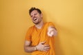Young hispanic man standing over yellow background laughing at you, pointing finger to the camera with hand over body, shame Royalty Free Stock Photo
