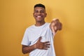 Young hispanic man standing over yellow background laughing at you, pointing finger to the camera with hand over body, shame Royalty Free Stock Photo