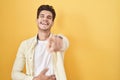 Young hispanic man standing over yellow background laughing at you, pointing finger to the camera with hand over body, shame Royalty Free Stock Photo