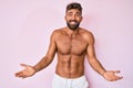 Young hispanic man standing shirtless clueless and confused expression with arms and hands raised Royalty Free Stock Photo