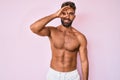 Young hispanic man standing shirtless doing ok gesture with hand smiling, eye looking through fingers with happy face