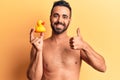 Young hispanic man standing shirtless holding duck toy smiling happy and positive, thumb up doing excellent and approval sign Royalty Free Stock Photo