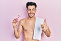 Young hispanic man standing shirtless holding razor smiling happy and positive, thumb up doing excellent and approval sign Royalty Free Stock Photo