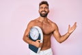 Young hispanic man standing shirtless holding weighing machine celebrating victory with happy smile and winner expression with Royalty Free Stock Photo