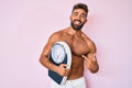 Young hispanic man standing shirtless holding weighing machine smiling happy pointing with hand and finger Royalty Free Stock Photo