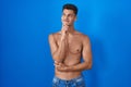 Young hispanic man standing shirtless over blue background with hand on chin thinking about question, pensive expression Royalty Free Stock Photo