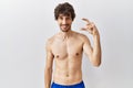 Young hispanic man standing shirtless over isolated, background smiling and confident gesturing with hand doing small size sign Royalty Free Stock Photo