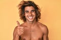 Young hispanic man standing shirtless smiling happy and positive, thumb up doing excellent and approval sign Royalty Free Stock Photo