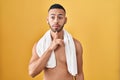 Young hispanic man standing shirtless with towel thinking concentrated about doubt with finger on chin and looking up wondering