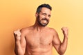 Young hispanic man standing shirtless very happy and excited doing winner gesture with arms raised, smiling and screaming for Royalty Free Stock Photo