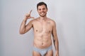 Young hispanic man standing shirtless wearing underware smiling and confident gesturing with hand doing small size sign with Royalty Free Stock Photo