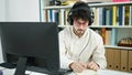 Young hispanic man student using computer and headphones writing notes at library university Royalty Free Stock Photo