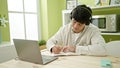 Young hispanic man student using computer taking notes wearing headphones at dinning room Royalty Free Stock Photo