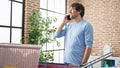 Young hispanic man talking on smartphone hanging clothes on clothesline at laundry room
