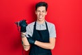 Young hispanic man tattoo artist wearing professional uniform and gloves holding tattooer machine doing ok sign with fingers, Royalty Free Stock Photo