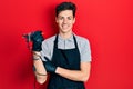 Young hispanic man tattoo artist wearing professional uniform and gloves holding tattooer machine looking positive and happy Royalty Free Stock Photo