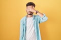 Young hispanic man with tattoos standing over yellow background covering eyes with hand, looking serious and sad Royalty Free Stock Photo
