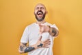 Young hispanic man with tattoos standing over yellow background laughing at you, pointing finger to the camera with hand over Royalty Free Stock Photo