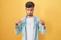 Young hispanic man with tattoos standing over yellow background pointing down looking sad and upset, indicating direction with Royalty Free Stock Photo