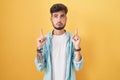 Young hispanic man with tattoos standing over yellow background pointing up looking sad and upset, indicating direction with Royalty Free Stock Photo