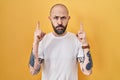 Young hispanic man with tattoos standing over yellow background pointing up looking sad and upset, indicating direction with Royalty Free Stock Photo